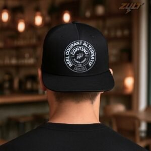 Casquette noire ZULT STAMP #3 Collection SIGNATURE avec imprimé circulaire “Courant Alternatif Continu” en blanc, portée par un homme dans un café, style graphique et urbain.